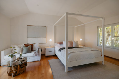 Modern bedroom with a four-poster bed, sofa, and side table.