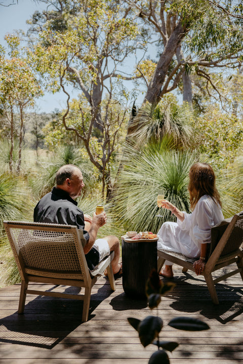 Two people sitting on a wooden deck in a natural setting, enjoying a meal together.