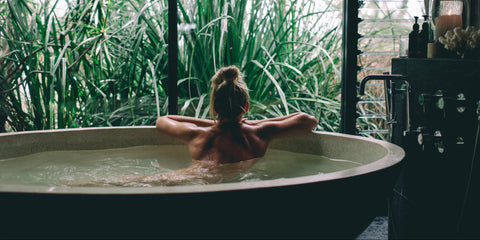 Person relaxing in a bathtub with lush greenery in the background