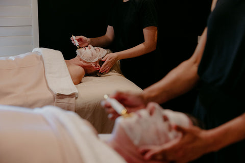 Couple receiving facials in a spa setting with therapists applying a roller.
