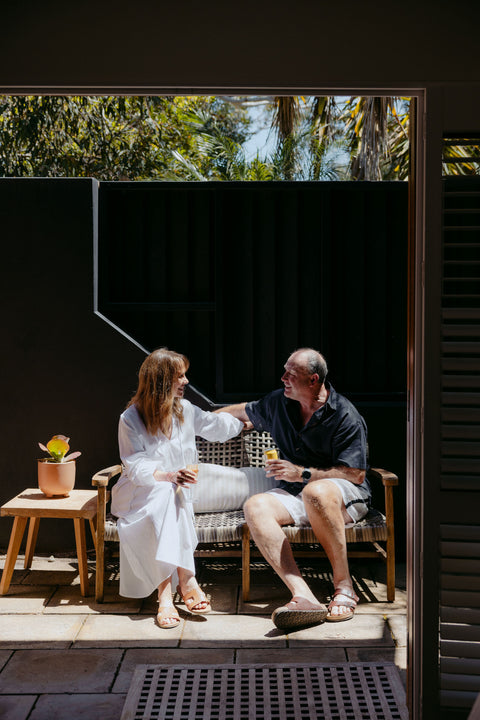 Couple sitting on a bench outdoors in a sunlit courtyard with dark walls