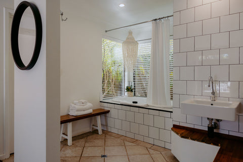 Bathroom with white tiled walls, a sink, and a window with blinds.
