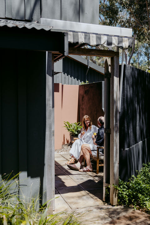 Two people sitting on a bench under a striped awning in a garden courtyard setting.