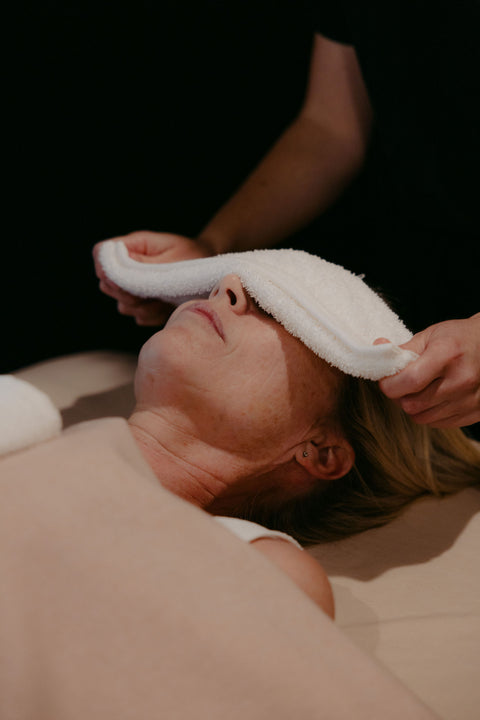 Person receiving a facial treatment with a towel on their face against a dark background