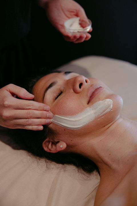 Person applying a facial mask to another person's face in a spa setting