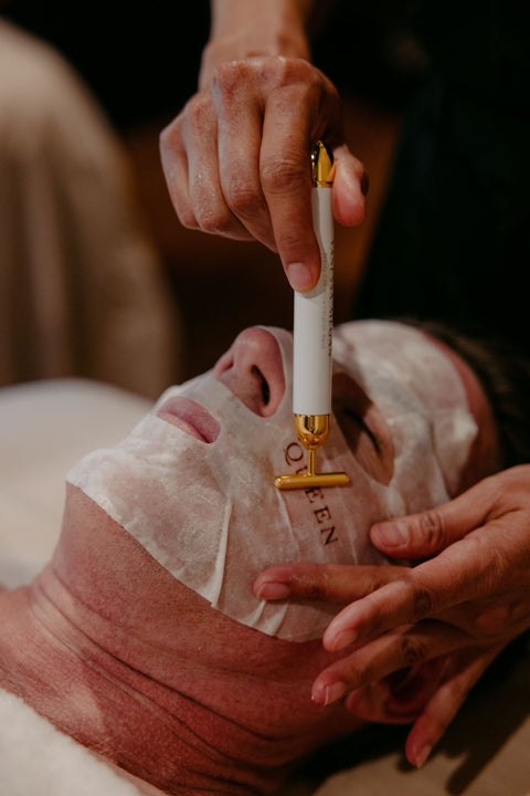 Person receiving a facial treatment with a white and gold tool on a dark background