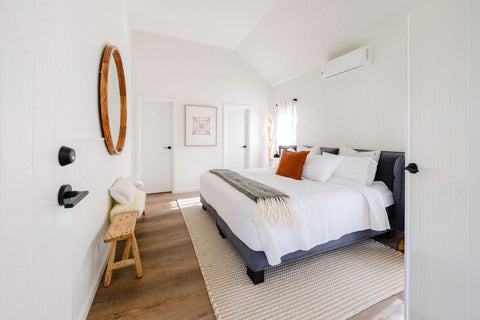 Modern bedroom with a bed, wooden stool, and round mirror.