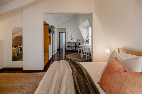 Bedroom with a bed and pillows, wall mirror reflecting living room, and open door to another room.