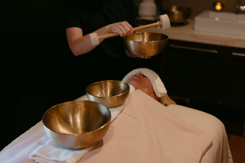 Person receiving a sound therapy treatment with metal bowls and a mallet.
