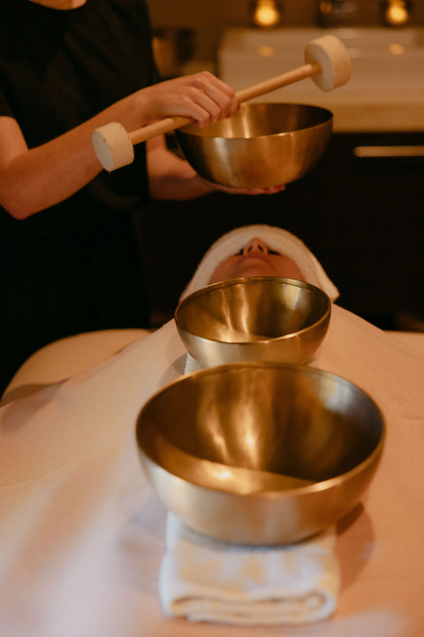 Person holding a wooden mallet over two metal bowls on a massage table.