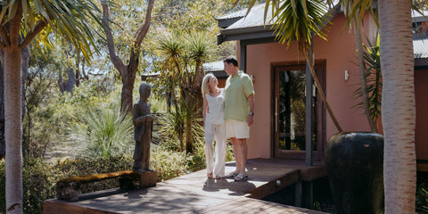 Man and woman standing on a wooden deck with palm trees and a building in the background