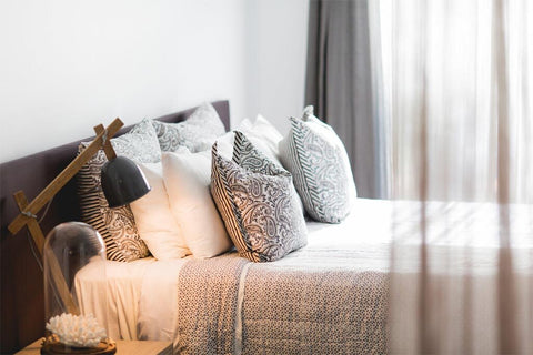 Decorative pillows on a bed with a lamp and plant in a bedroom setting
