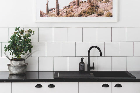Modern kitchen with black faucet, plant, and framed picture on white tiled wall.