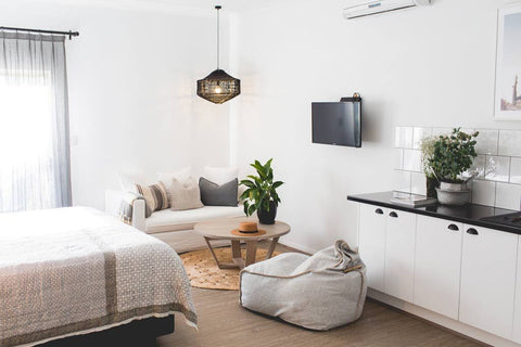 Modern bedroom with white walls, a bed, sofa, and kitchen area.