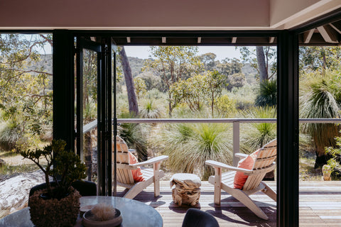 Outdoor patio area with wooden chairs, a small table, and plants, featuring a view of trees and nature.