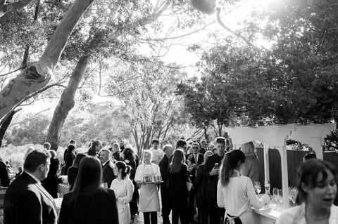 Black and white photo of a group of people at an outdoor event with trees in the background.