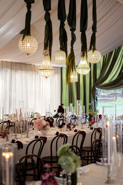Decorative table setting with hanging lights and floral arrangements in a room with green curtains.