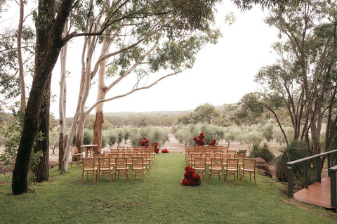 Outdoor wedding setup with chairs and floral arrangements in a natural setting.